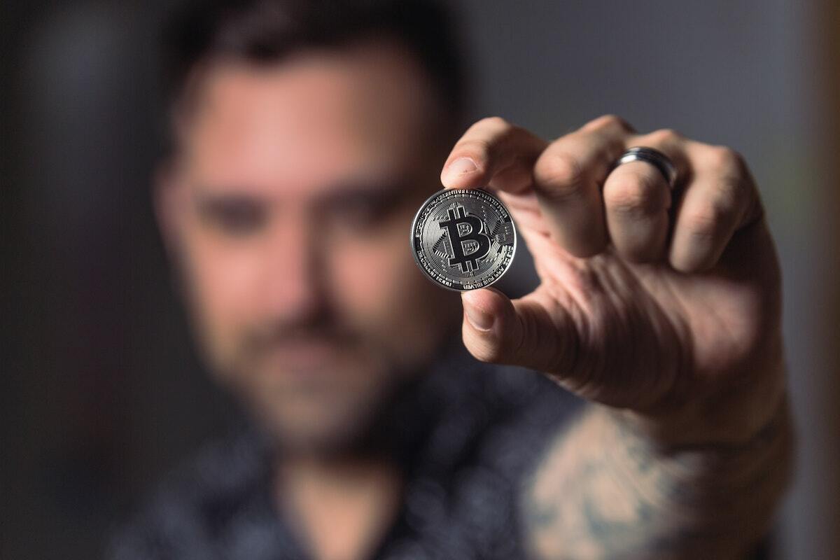 man holding up coin with bitcoin logo